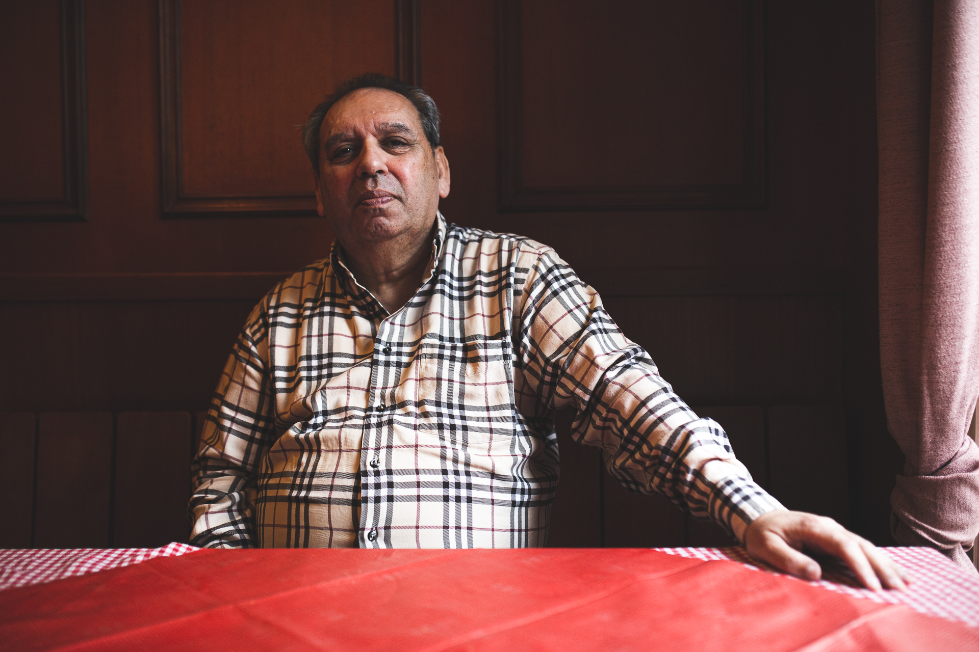 Ricardo Lenzi Laubinger sitzt an einem Tisch, der mit einer roten Tischdecke bedeckt ist und schaut ernst in die Kamera. Er trägt ein kariertes Hemd.