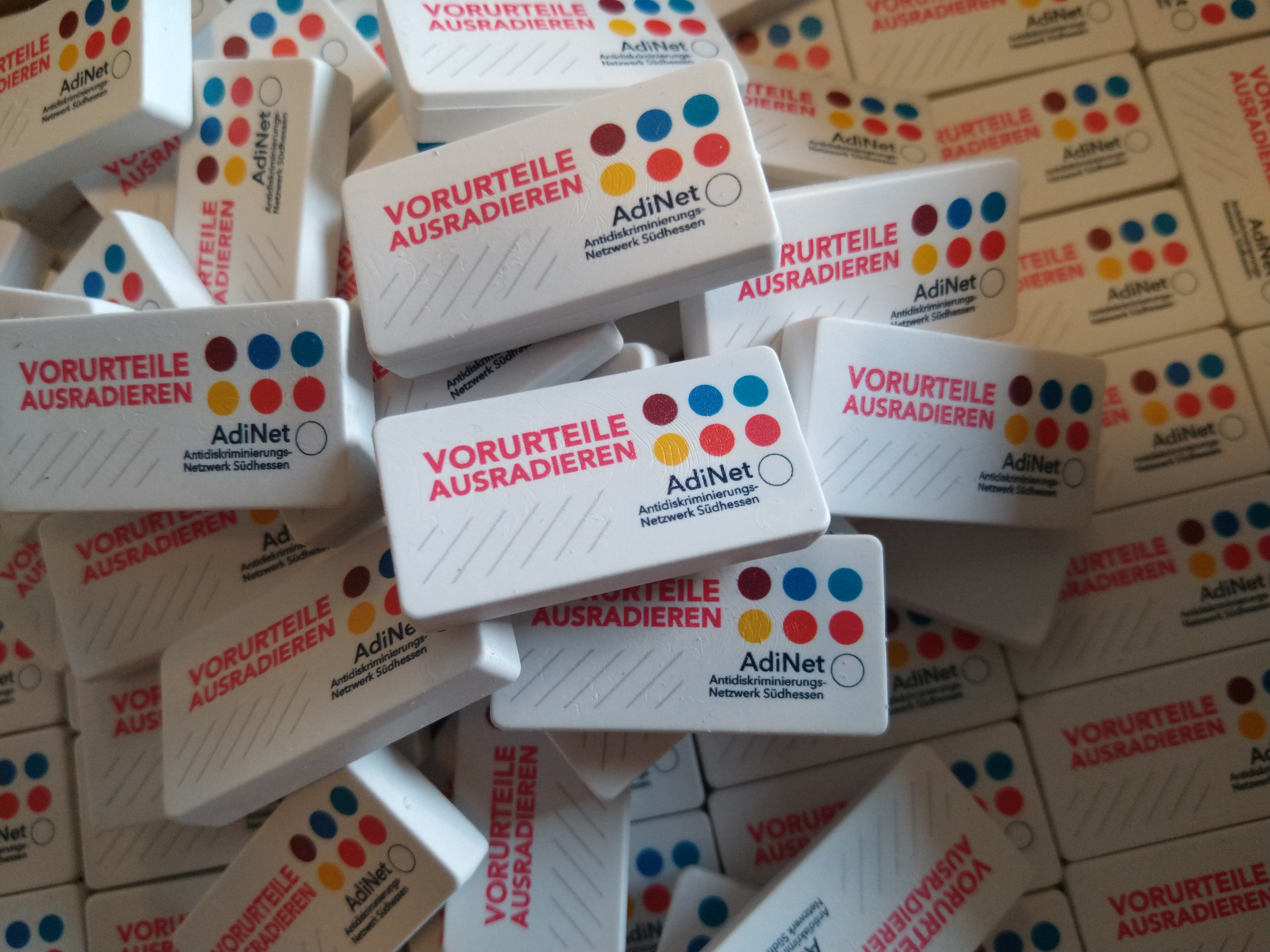 Häufchen aus bedruckten Radiergummis mit der Aufschrift "Vorurteile ausradieren" und dem Logo des Antidiskriminierungs-Netzwerks Südhessen.